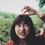 A young woman playfully holds a flower outdoors, expressing joy and charm.